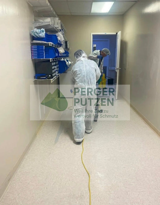 Professional cleaners in protective suits cleaning a hallway in a medical or office building